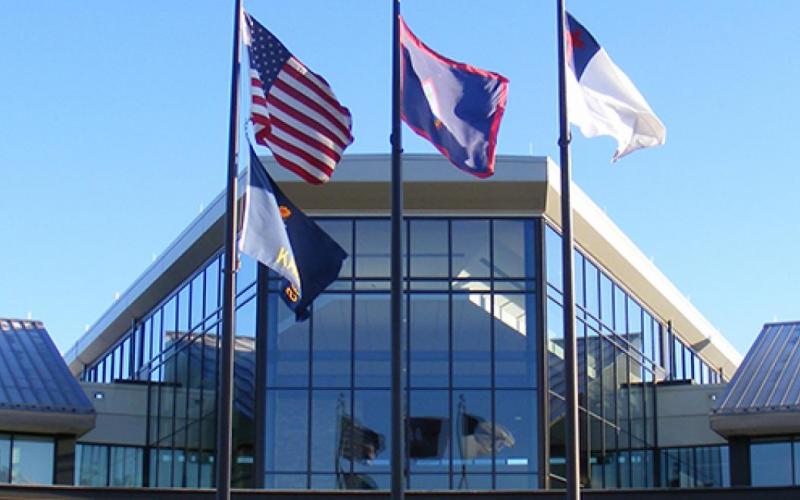 En el centro de la bandera de Guam está su escudo de armas, un emblema en la forma de almendra que representa un vela proa navegando en Agana Bay y GUAM en letras rojas. La forma del emblema recuerda las piedras de lanza utilizadas por los ancestros de los isleños. La forma de relieve en la parte de atrás representa el despeñadero Punta Dos Amantes en Guam. 