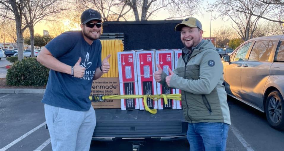 Two men smile in front of a pickup truck.